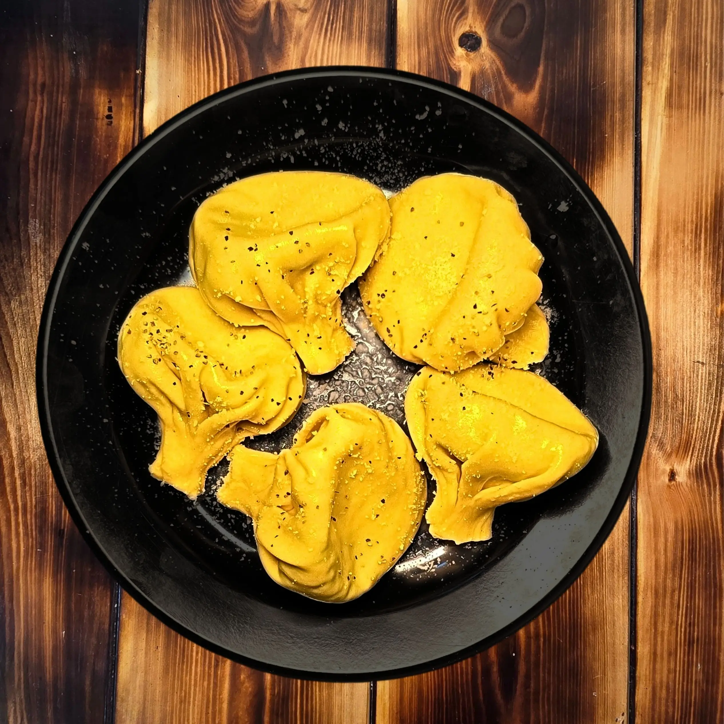 חמישה כיסוני חינקלי צהבהבים במילוי גבינה מונחים על צלחת שחורה, מעוטרים במעט תבלינים