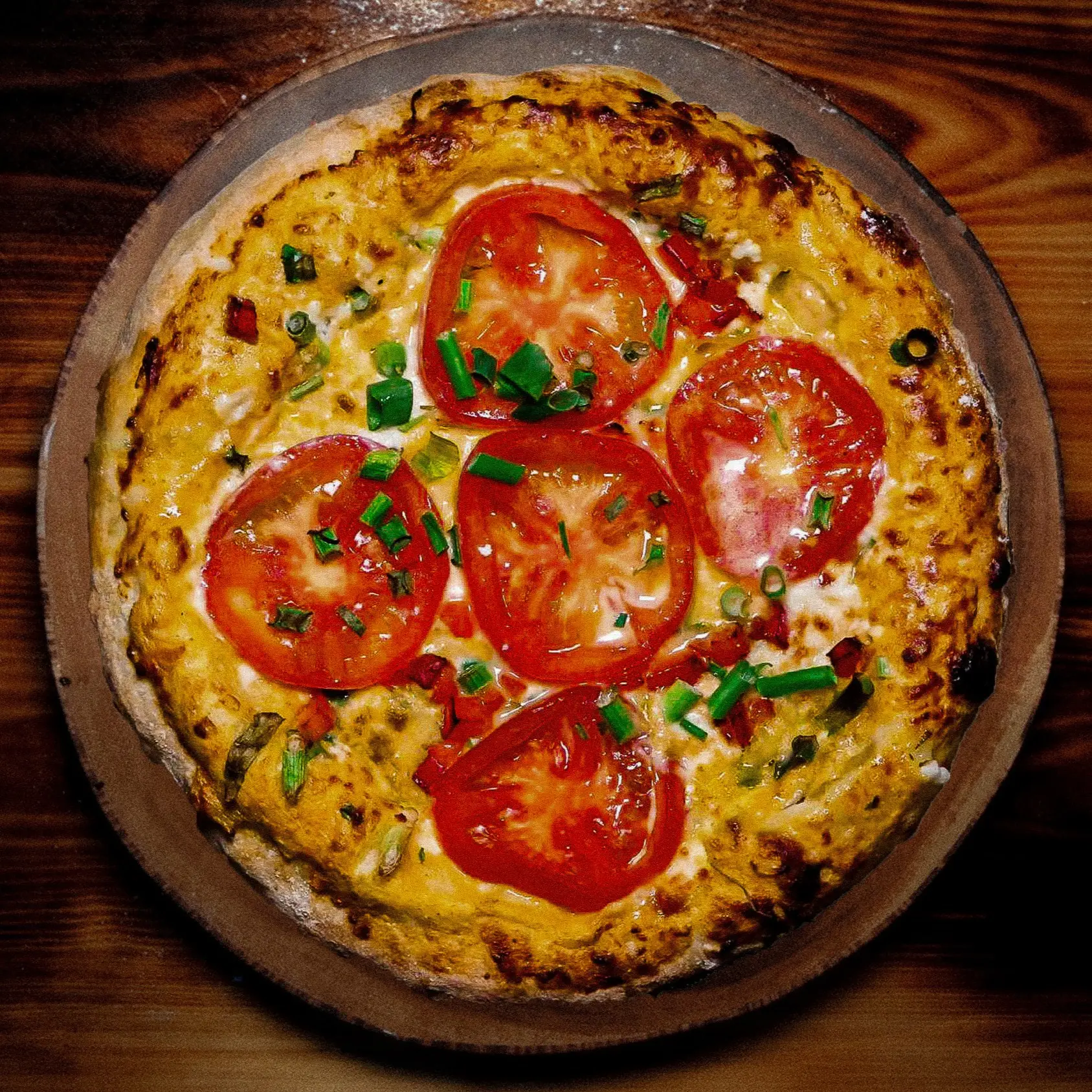 מאפה עגול וזהוב המכוסה בשכבת גבינה ועליו מסודרות פרוסות עגבנייה גדולות ועירית קצוצה.